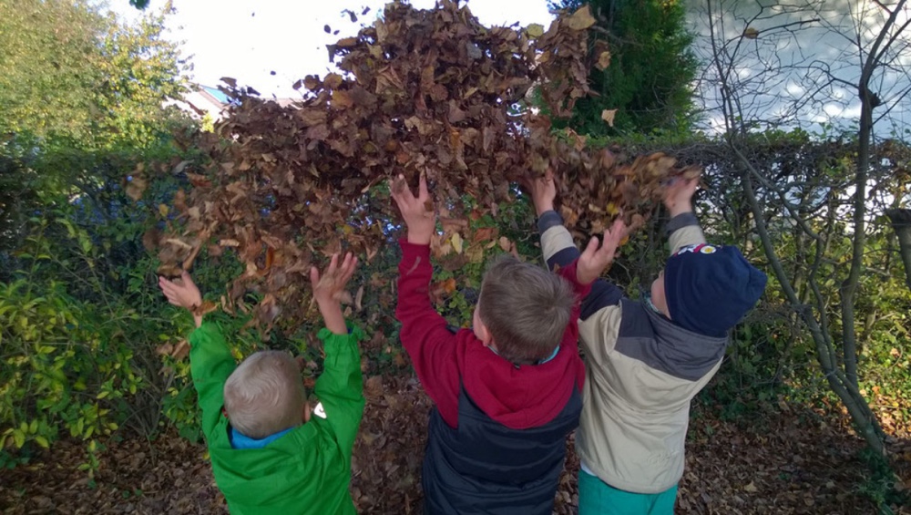Drei Kinder werfen gemeinsam Herbstlaub in die Luft